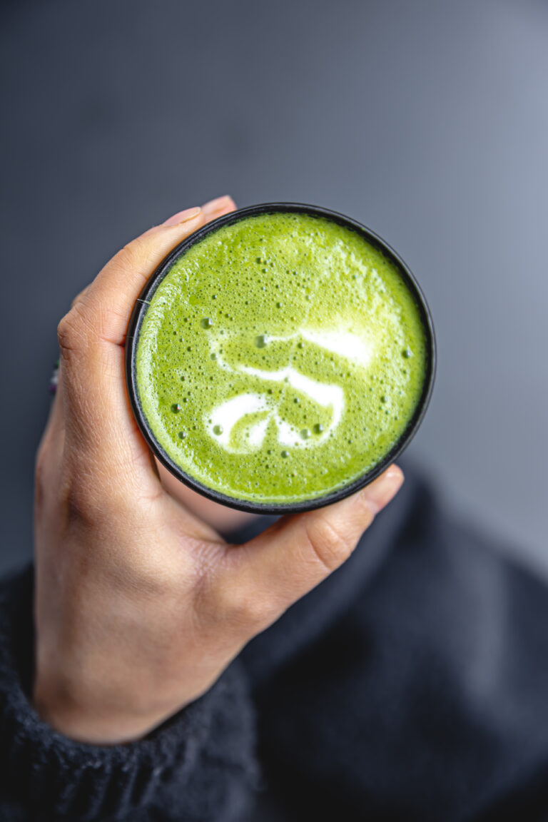 Top view of woman holding in hands trendy green matcha drink with latte art